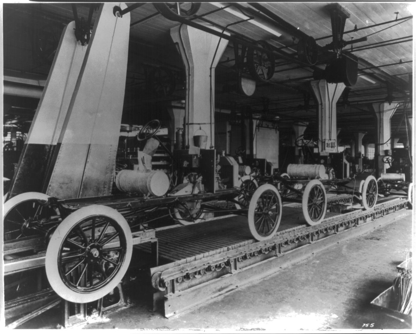 Workers along Ford's Highland Park assembly line, attaching parts to car chassis moving past them